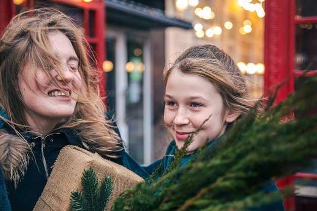 A little girl and young woman with thuja branches and a gift under a plaid