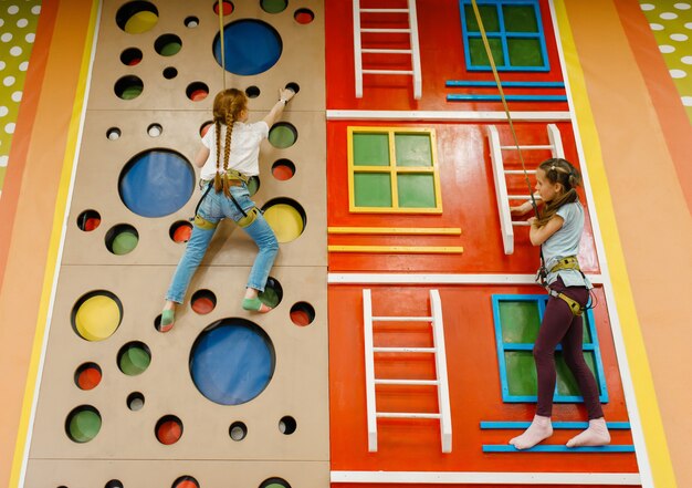 Foto piccole amiche sulla parete da arrampicata nel centro di intrattenimento. svaghi delle bambine in vacanza, felicità infantile, bambini felici nel parco giochi