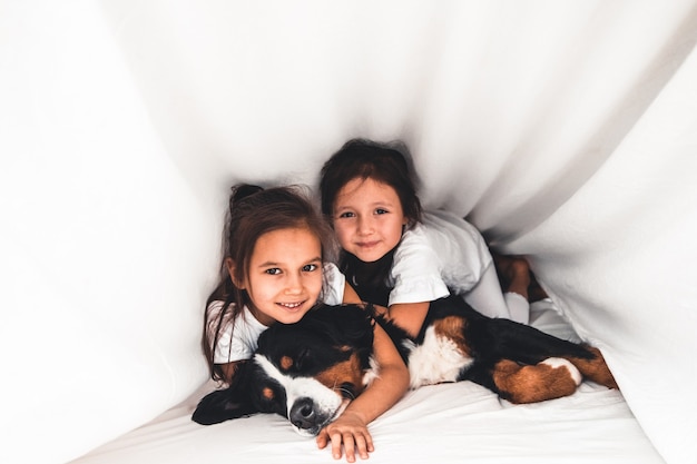 Little girls in bed with dog Bernese Mountain Dog, friendship