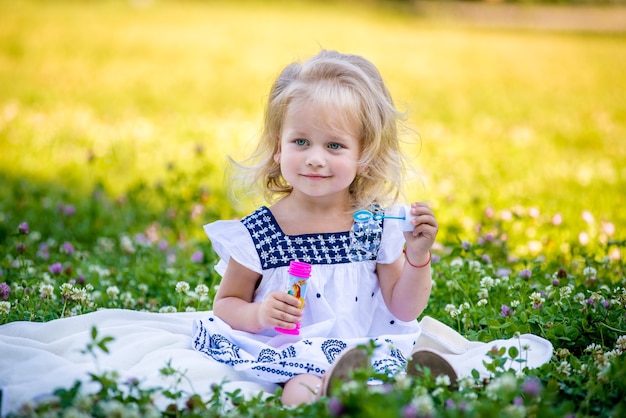 Little girls blow bubbles sitting on the grass