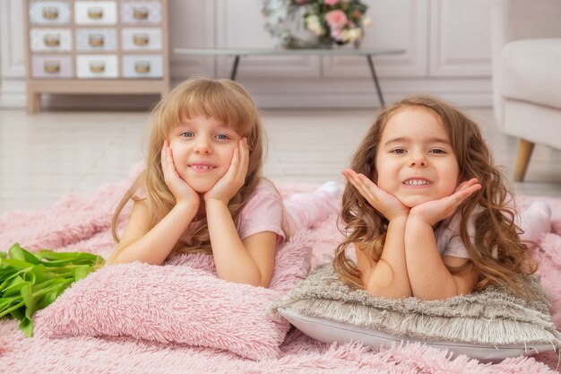 Little girls of Caucasian appearance are playing while sitting on the floor in a bright living room in a Scandinavian style with a bouquet of flowers