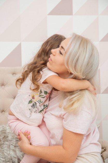 Bambine dall'aspetto caucasico abbraccia teneramente sua madre in un luminoso soggiorno in stile scandinavo