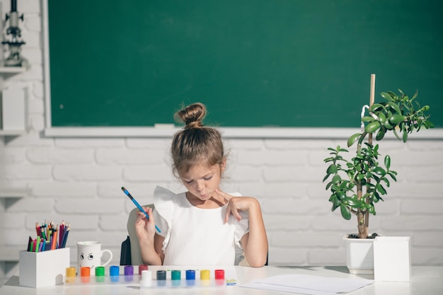 学校の教室の子供たちの創造的な成長で鉛筆クレヨンでカラフルな絵を描く小さな女の子