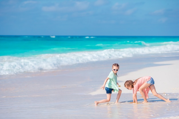 Little girls having fun at tropical beach playing together at shallow water