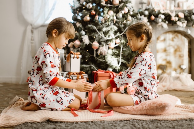 写真 パジャマ姿の女の子がクリスマスツリーの下にギフトボックスを開く