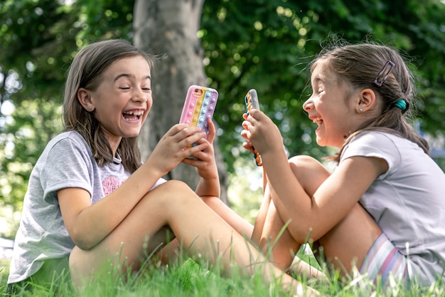 にきびのあるケースに携帯電話を持っている屋外の小さな女の子がそれをポップします、流行の抗ストレスおもちゃ。