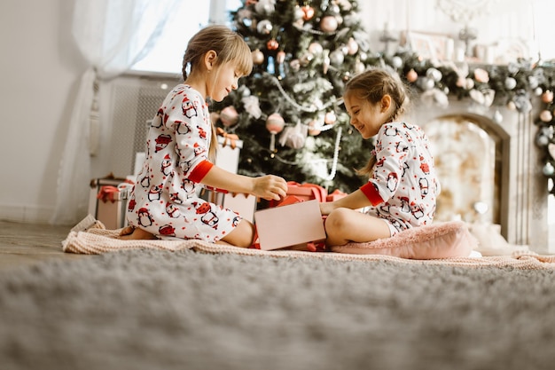 Little girls in pajamas open gift box under the Christmas tree