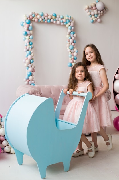 Маленькие девочки в розовых платьях играют с голубой коляской, как маленькие мамы