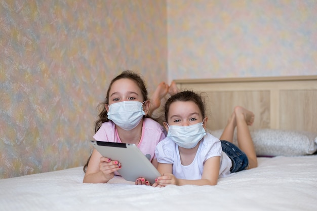 Photo little girls in protective masks playing on a tablet