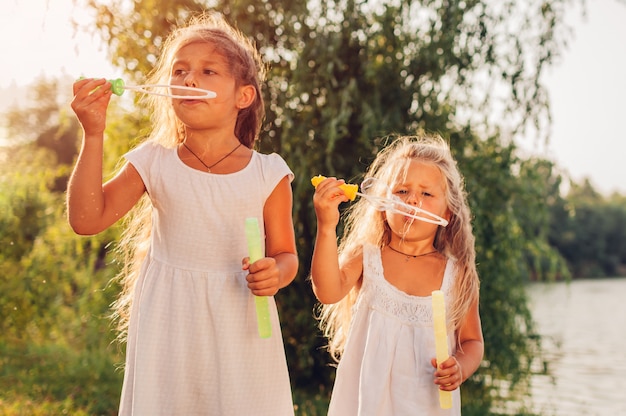 Little girls sisters blowing bubbles in spring park. Kids having fun playing games outdoors.