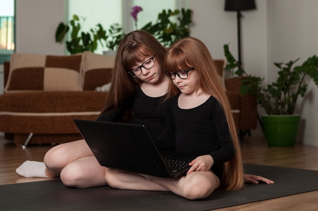 Little girls sisters hold an online lesson gymnastics at home