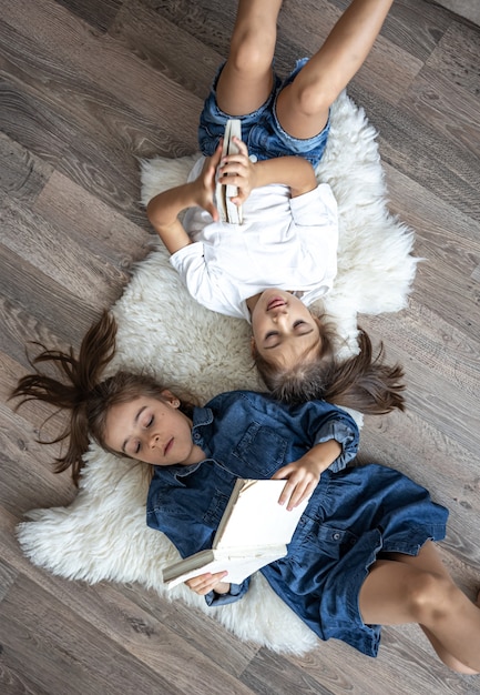 Сестры маленькие девочки читают книги, лежа на полу, вид сверху.