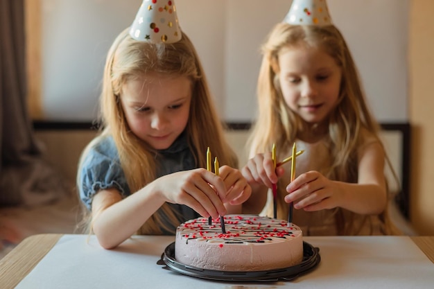 小さな女の子の姉妹の双子は、キャンドルでバースデーケーキを飾ることができます自家製の休日の帽子子供の誕生日のお祝い病気の検疫隔離中に屋内パーティー