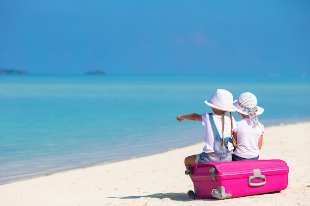 Foto bambine con la grande valigia e mappa alla spiaggia tropicale