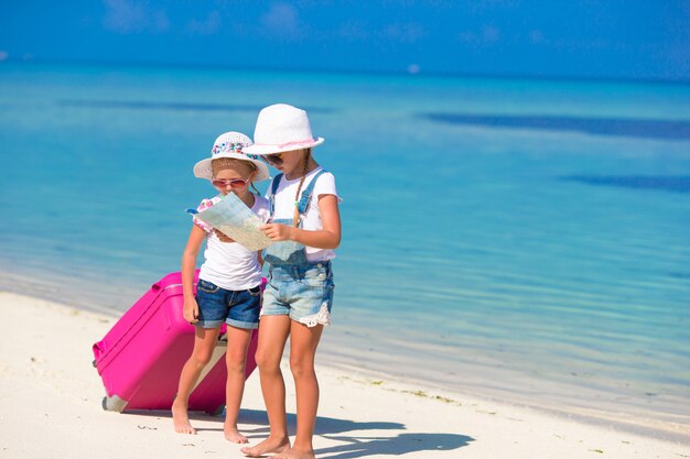 Маленькие девочки с большим чемоданом и картой на тропическом пляже