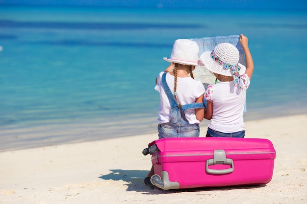 Little girls with big suitcase and map at tropical beach