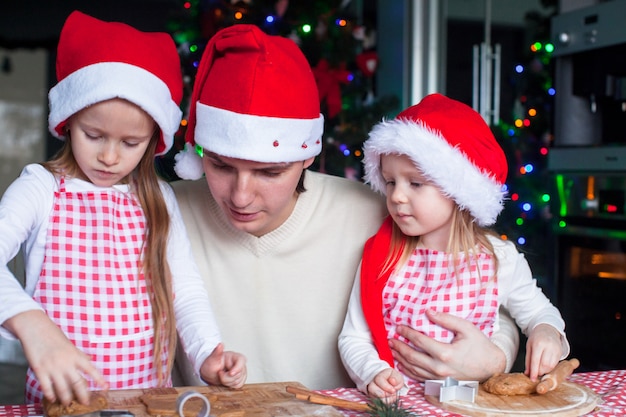 サンタ帽子の若いお父さんと小さな女の子がクリスマスジンジャーブレッドクッキーを焼く