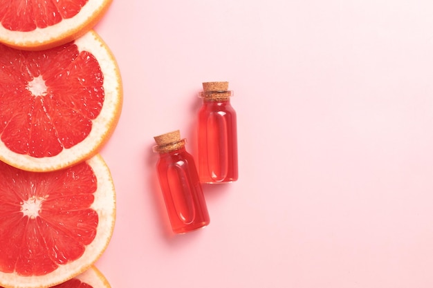 Little glass vial of aroma essential oil wich grapefruit fresh slice Flat lay top view face serum in bottle on pink table SPA relax face skin care and body treatment