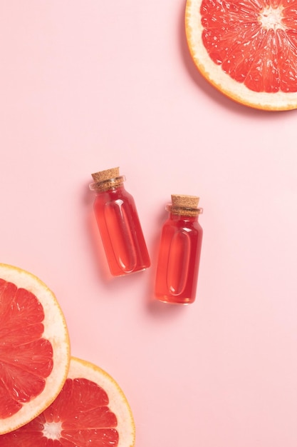 Little glass vial of aroma essential oil wich grapefruit fresh slice Flat lay top view face serum in bottle on pink table SPA relax face skin care and body treatment