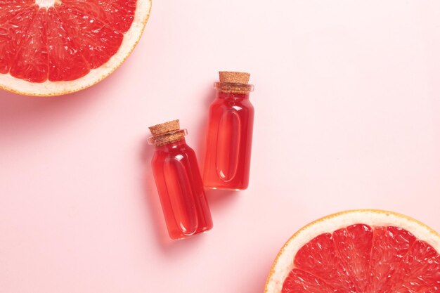 Little glass vial of aroma essential oil wich grapefruit fresh slice Flat lay top view face serum in bottle on pink table SPA relax face skin care and body treatment