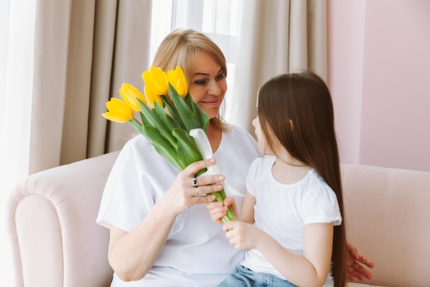 A little granddaughter gives her grandmother a bouquet of tulips A happy family The concept of gratitude love wellbeing