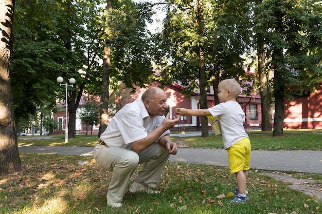 Photo a little grandson in yellow shorts carefully and lovingly feeds a balding grandfather with popcorn from a yellow glass in an amusement park