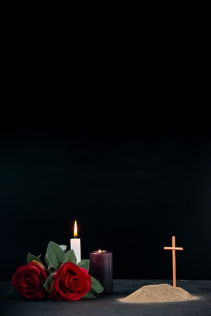 Little grave with candle and flowers as memory on dark surface