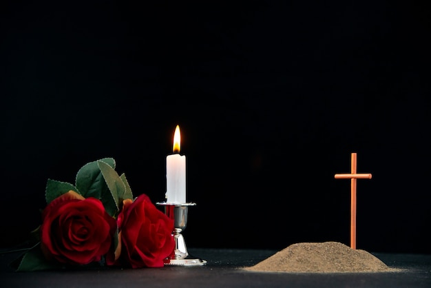 Little grave with candle and flowers as memory on dark surface