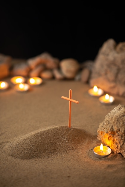 Little grave with stones and burning candles on dark surface