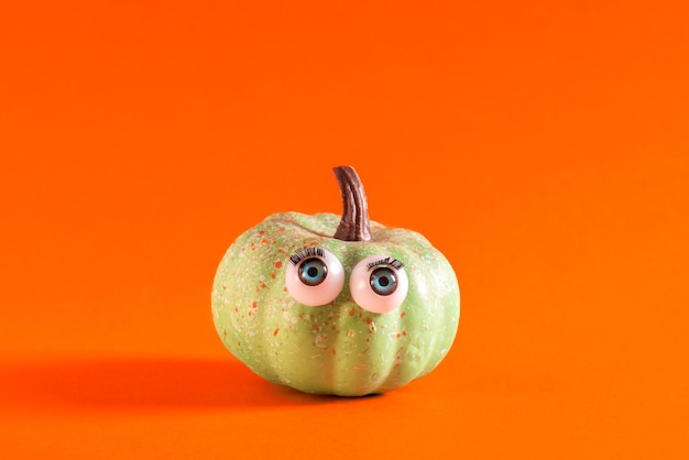 Little green pumpkin with googly eyes on orange background