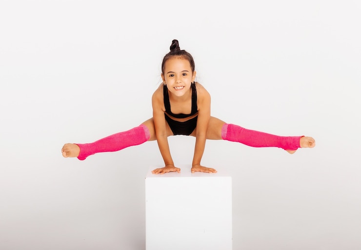 Photo little gymnast on a large white cube performs sports exercises
