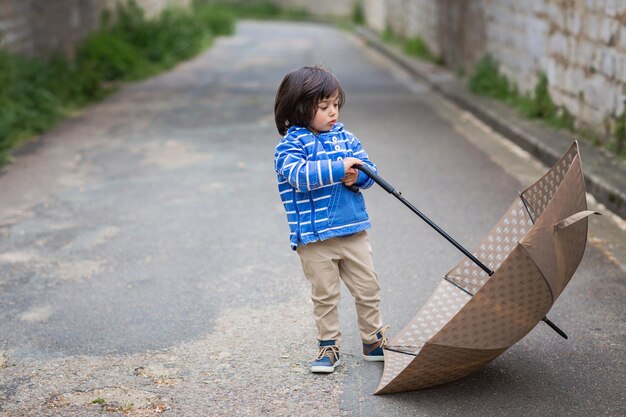 Маленький красивый мальчик играет с зонтиком на открытом воздухе