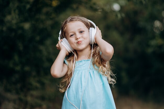 A little happy blonde cute girl listen to music with hands on her big white headphones