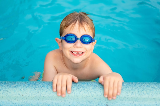 スイミンググラスの小さな幸せな男の子の子供は、ウォーターパークで夏の水泳トレーニング夏の子供たちの週末の子供たちの休暇の子供でプールで泳ぐことを学びます