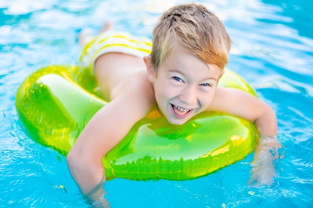 어린 행복한 소년 아이는 여름 여름 어린이 주말 어린이 방학 동안 고무 팽창식 원으로 수영장에서 수영합니다.