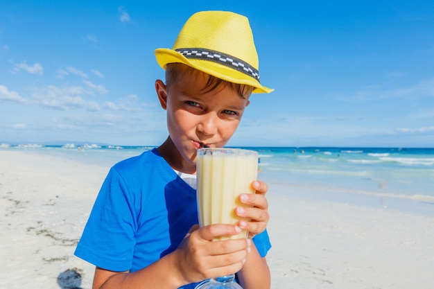 Little happy boy drinking banana cocktail on tropical beach