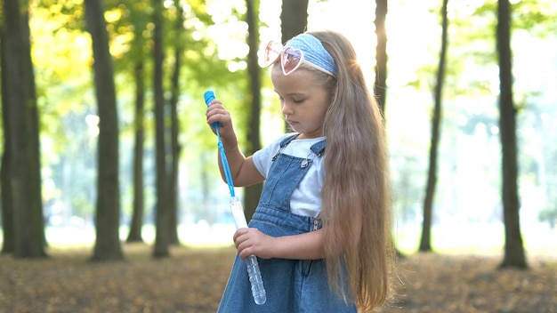 緑の公園でシャボン玉を吹く小さな幸せな子の女の子。屋外の夏の活動のコンセプト。