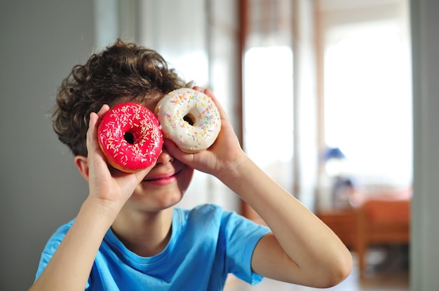 Il piccolo ragazzo sveglio felice osserva attraverso le ciambelle