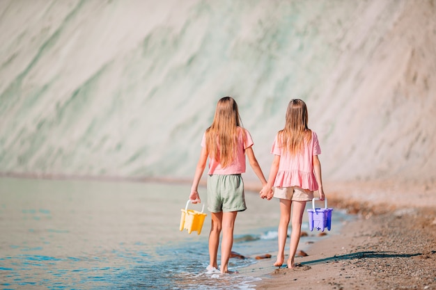 Little happy funny girls have a lot of fun at tropical beach playing together. Sunny day with rain in the sea