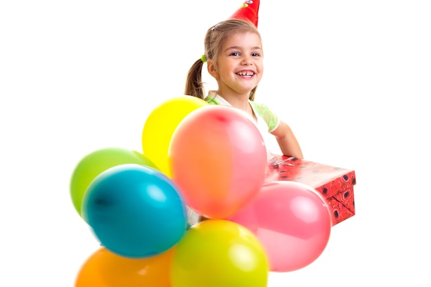 Little happy girl celebrating birthday with multicolor ballons and red box with gift.