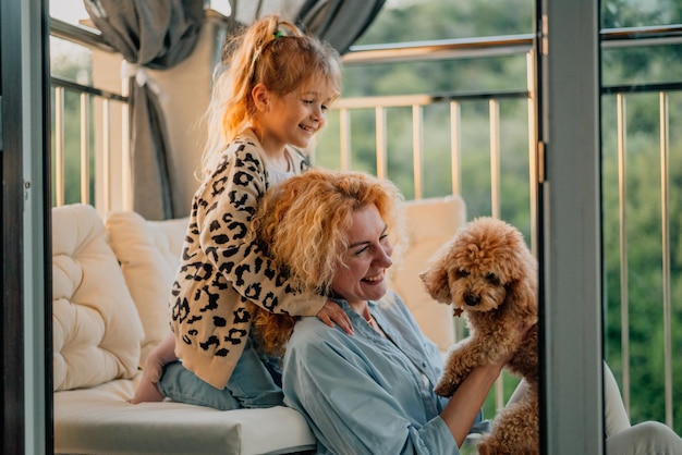 Una bambina felice un bambino con un sorriso gioca in una vernada primaverile estiva a casa con mamma e un cane al tramonto weekend in famiglia sera cane animali domestici come membro della famiglia