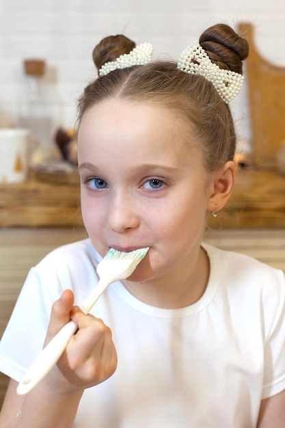 La bambina felice decora i biscotti di pan di zenzero di natale usando il fuoco selettivo della glassa rossa