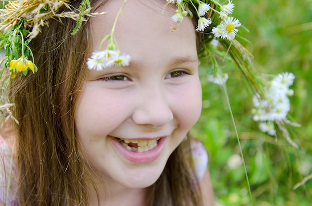 Little happy girl in a garland of field flowers in the meadow