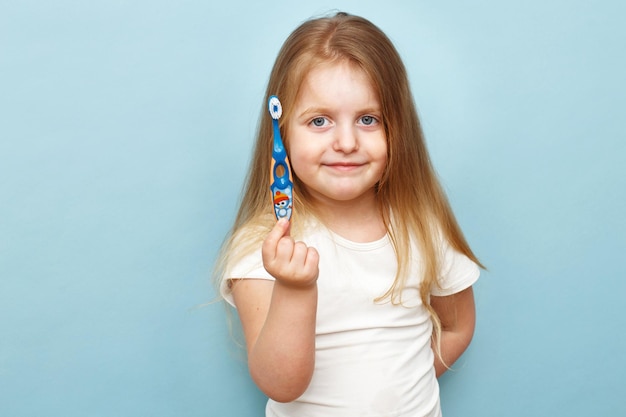 Маленькая счастливая девочка держит зубную щетку и улыбается на синем фоне