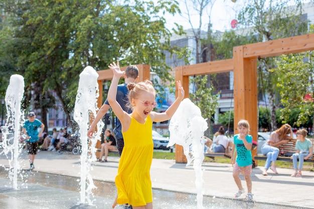 Маленькая счастливая девочка бежит возле фонтана летом в парке