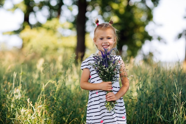 Little happy girl in a striped dress holding a bouquet of flowers