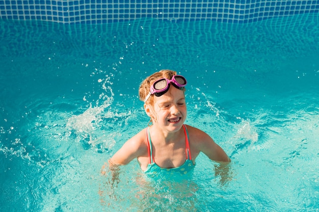 little happy girl swims in the pool. summer holidays. girl in a swimsuit and swimming glasses.