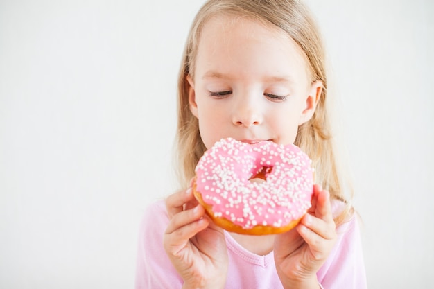 Little happy girl with blond hair playing and tasting donuts with pink icing at hanukkah celebration