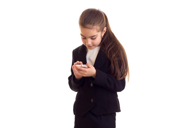 Little happy girl with long chestnut ponytail in black jacket and black skirt talking on the phone