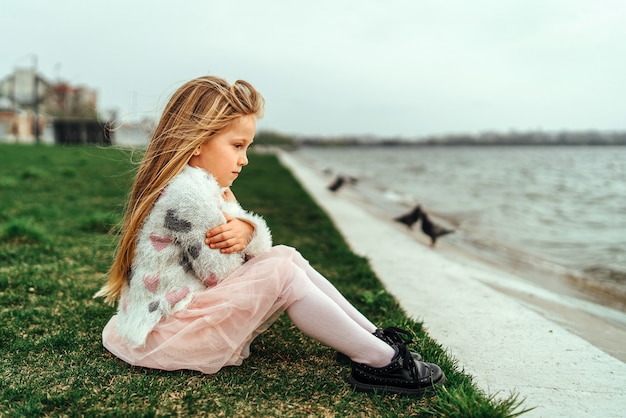 Little happy pretty girl sitting near lake in the park